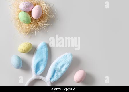 Easter bunny ears, nest and pastel colorful eggs on gray background. View from above. Flat lay. Happy spring greeting card with copy space. Stock Photo