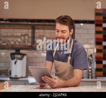 Sending out special offers to all my existing customers. Shot of a young man using a digital tablet while working in a coffee shop. Stock Photo