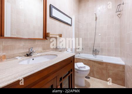 A corner shot of a bathroom with a white porcelain sink set on a marble countertop over dark wood to match the mirror Stock Photo