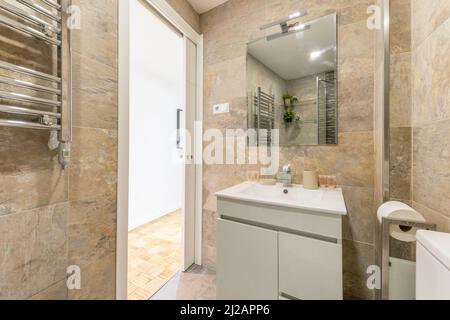 bathroom with white porcelain on white wooden sink with frameless mirror, marble tiling and chrome heated towel rail in vacation rental apartment Stock Photo