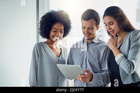 The collaborative team is a productive team. Shot of a group of young businesspeople using a digital tablet together in a modern office. Stock Photo