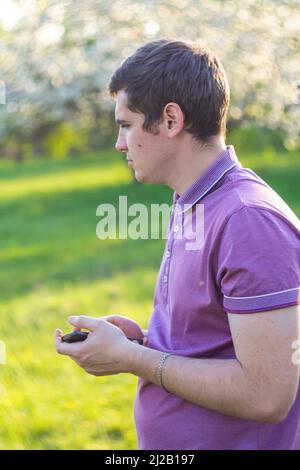 Defocus pleasant cheerful handsome young man holding phone. Profile view. Nature green garden background. Mindfulness concept. Mental health. Psycholo