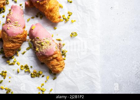 Mini-croissants with ruby chocolate and pistachios on a baking paper, gray background. Top view and copy space. Stock Photo