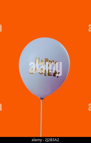 closeup of a blue balloon with the text happy easter written in it, on an orange background with some blank space on top Stock Photo