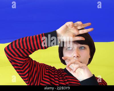 frightened teenage girl covers her head with her hands against the background of the Ukrainian flag. Stock Photo