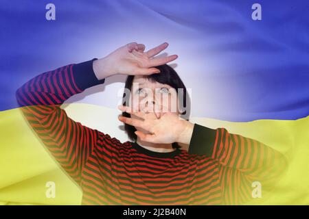 frustrated frightened teenage girl in a panic covers her head with her hands against the background of the ukrainian flag. Stock Photo