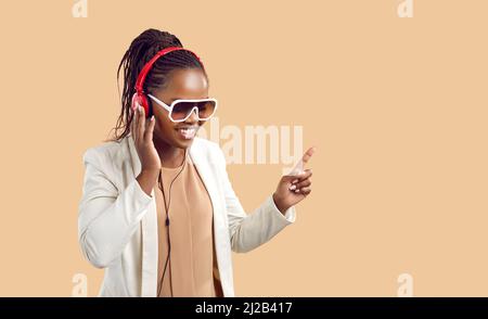 Happy young african american woman in headphones listens to music on beige background. Stock Photo