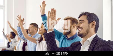 Group of happy people raising their hands up to ask questions at business conference Stock Photo