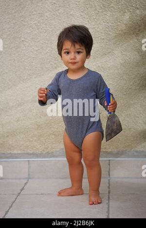 Portrait of a little eastern handsome baby boy playing outdoor with tool spatula Stock Photo