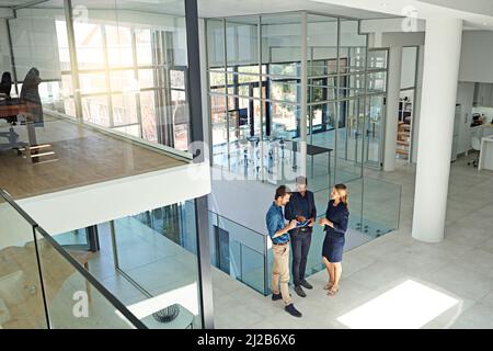 Contemporary business needs modern thinkers. Shot of three colleagues talking together over a digital tablet while standing in a modern office. Stock Photo