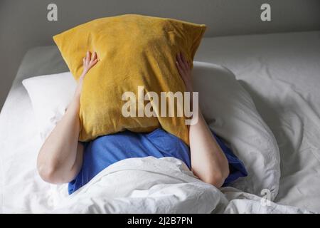 tired listless person lying in bed and hiding face under pillow Stock Photo