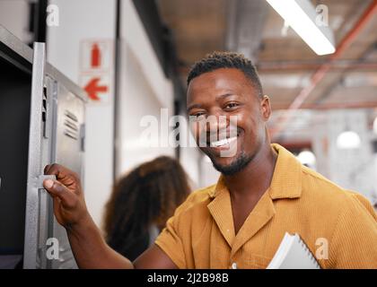 A young black student smiles at the camera and opens his locker on campus Stock Photo