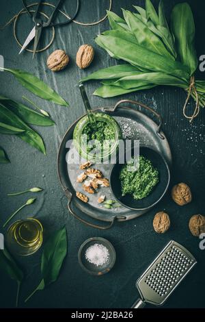 Homemade wild garlic pesto on a metal tray, wild garlic leaves, salt, oil and walnuts on dark green background, top view Stock Photo