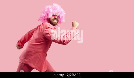 Funny clown in pink wig, suit and sunglasses running isolated on pink color background Stock Photo