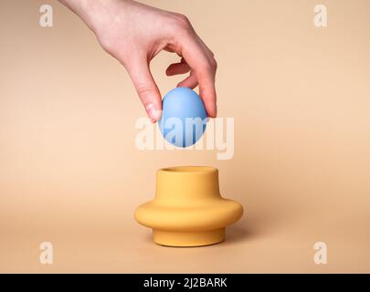 Hand putting blue dyed egg in cup. Holder and server on beige background. Easter celebration tradition concept. High quality photo Stock Photo