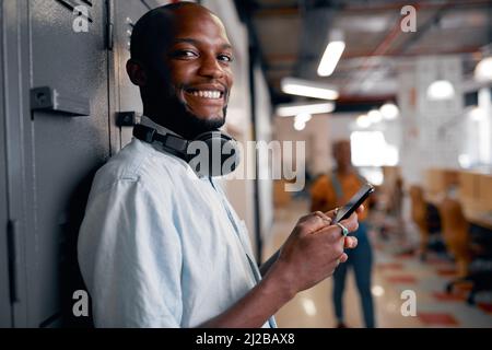 A young black man smiles at the camera on his mobile phone at university lockers Stock Photo
