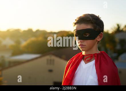 The city needs him. Shot of a young boy in a cape and mask playing superhero outside. Stock Photo