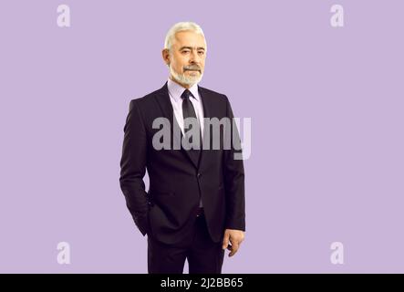 Elegant handsome senior businessman in classic suit isolated on purple background Stock Photo