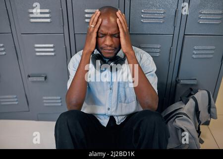 A young black student sits on the floor head in hands, feeling upset at college Stock Photo