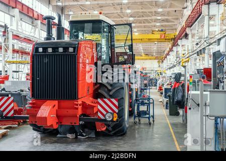 Big red harvester or tractor in process of being assembled on production line at factory for production manufacturing of agricultural machinery. Stock Photo