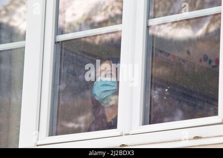 Elementary school during the Covid-19, Coronavirus outbreak: schoolgirl wearing a face mask looking through a window in a classroom Stock Photo