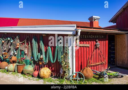 Discarded maritime objects and equipment such as rusted buoys and old fishing nets displayed on the wooden wall of a shed in Nordkoster. Stock Photo