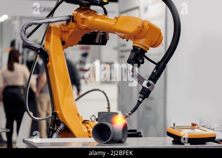 Closeup yellow arm robot welding metal pipe part in industry factory. Stock Photo
