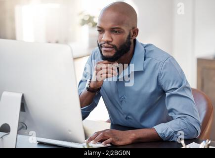 Ive gotta give this some thought. Cropped shot of a handsome young businessman looking thoughtful while working on his computer in the office. Stock Photo