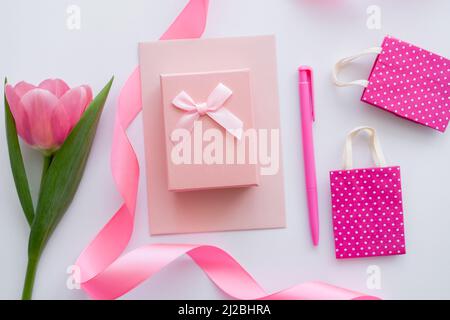 top view of gift box on envelope near pink tulip and shopping bags on white Stock Photo