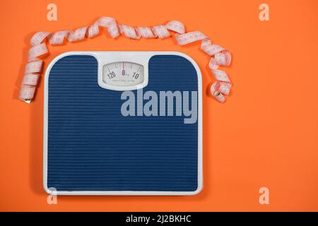 Floor blue scales and centimeter measuring tape on an orange background, top view. The concept of weight loss and weight control Stock Photo