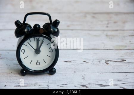 Black alarm clock isolated on wooden desk. The clock set at 1 o'clock. Stock Photo