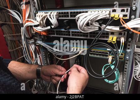 IT technician handling fiber optic cables from a communications cabinet Stock Photo