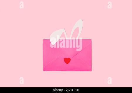 Paper rabbit ears behind of a pink envelope on a pink background with copy space Stock Photo