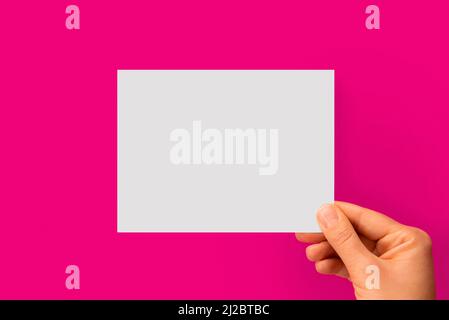 Woman's hand holding white blank paper on a pink background Stock Photo