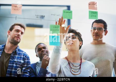 Put your plans out there. Shot of a group of designers brainstorming with notes on a glass wall in an office. Stock Photo