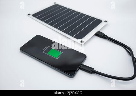 Smartphone charging with portable solar photovoltaic panel,renewable green energy tech Stock Photo