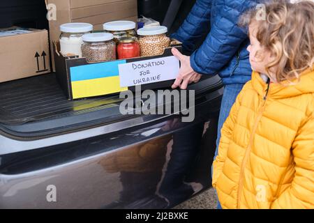 Mother and son taking a box with food to donate to Ukrainian refugees. Humanitarian aid in the Ukrainian war Stock Photo