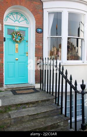 Stone steps of a house leading up to a bright turquoise front door, decorated with a colourful Easter wreath. With a bay window. Weymouth, Dorset, UK. Stock Photo