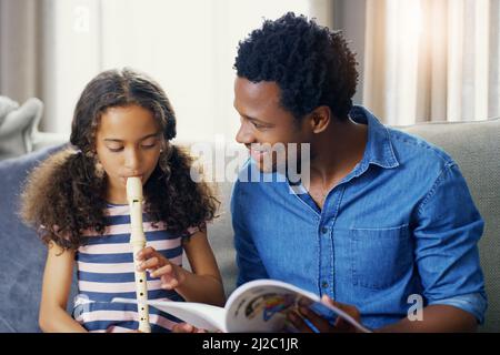 Fathers are often the first teachers in their childrens lives. Shot of a young father teaching his daughter how to play the recorder at home. Stock Photo