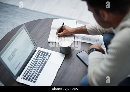 The most important step in your plan is sticking to it. Shot of a young man using a laptop and writing in a notebook while working from home. Stock Photo
