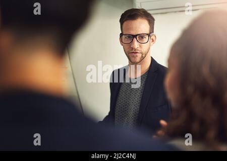 Leading his team by example. Shot of a young man giving a presentation to colleagues in an office. Stock Photo