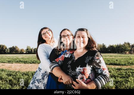 Grandmother, mother and daughter laughing and hugging in the field on a sunny day afternoon. Family portrait. Stock Photo