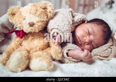 Infant multiethnic baby boy sleeping on a bed. Looking cozy with teddy bear Stock Photo