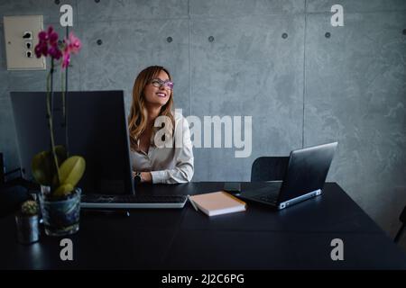 Merry, an adult woman, with glasses, looks out the window and thinks. She sits at her desk. Stock Photo