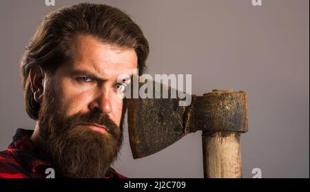 Bearded man with old axe near face. Brutal lumberjack hipster with ax. Closeup portrait. Stock Photo