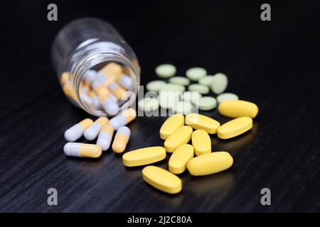 Pills on a dark wooden table, variation of medication in capsules and tablets scattered from a bottle. Concept of pharmacy, antibiotics, vitamins Stock Photo