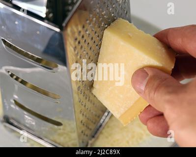 male hand grating Parmesan cheese on a metall kitchen grater, closeup of using a grater Stock Photo