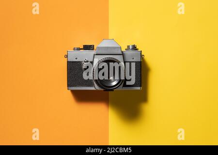 Retro analogue camera. Vintage old fashioned camera with lens on two colored background. Top view. Stock Photo