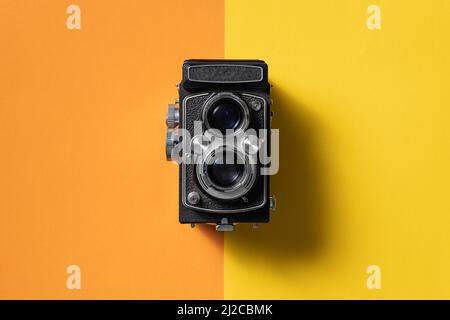 Retro analogue camera. Vintage old fashioned camera with lens on two colored background. Top view. Stock Photo