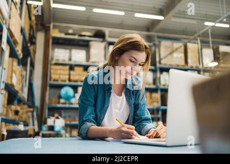 Woman using laptop at warehouse Stock Photo
